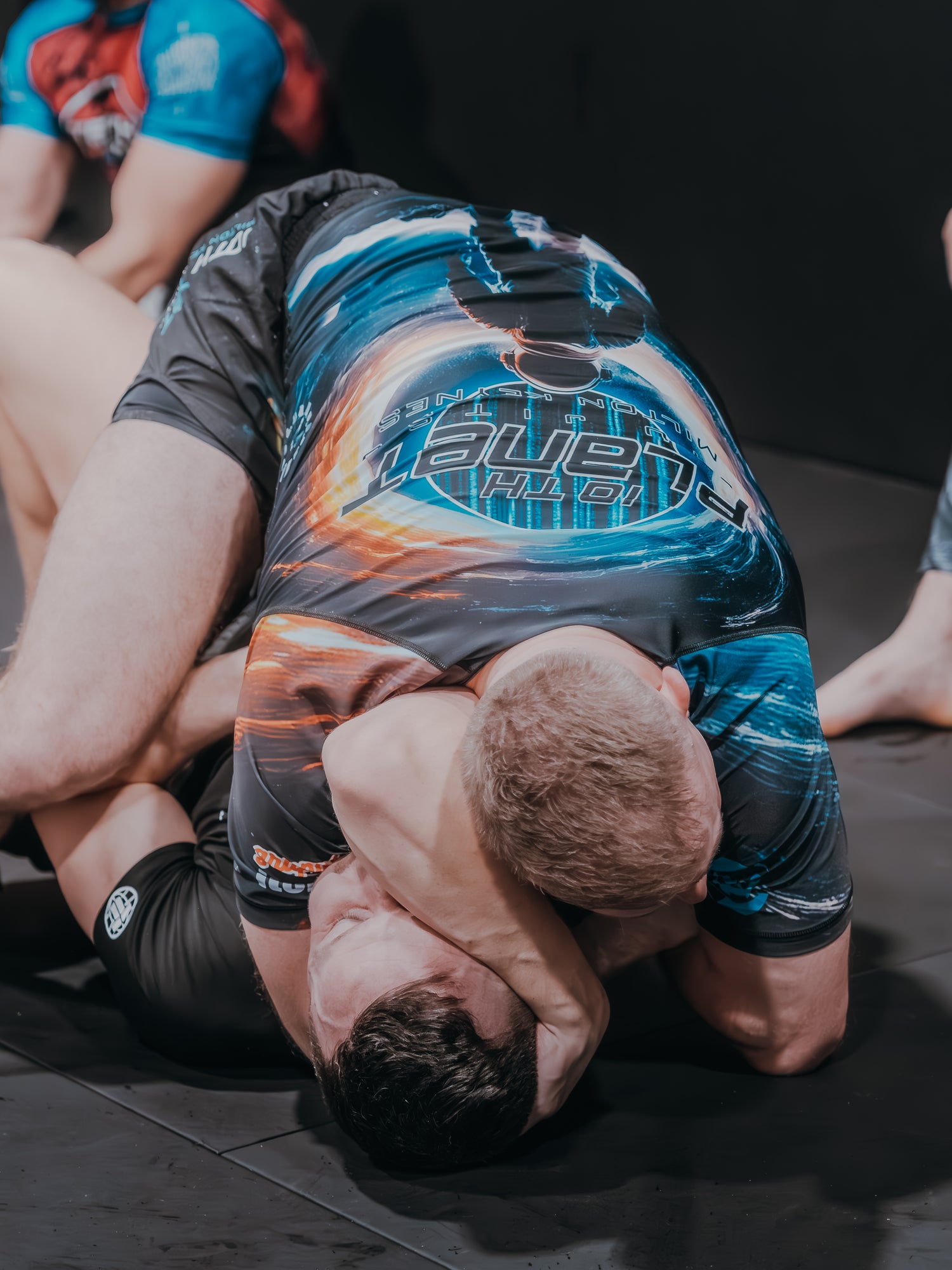 Two individuals in grappling positions on a mat, wearing colorful athletic outfits.