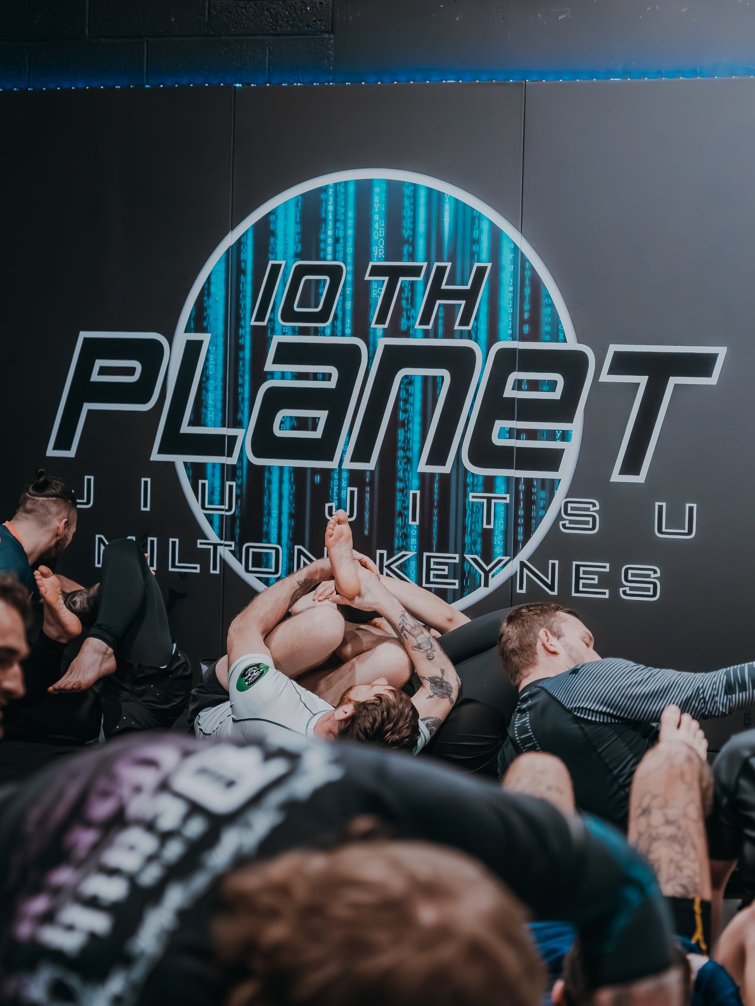 10th planet milton keynes logo on a padded wall with athletes grappling.