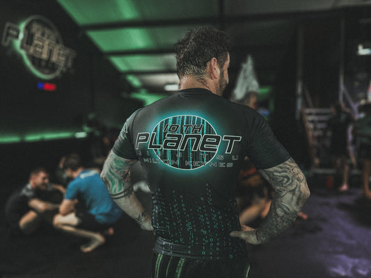 Person wearing a black rash guard with '10th Planet' logo in a gym setting